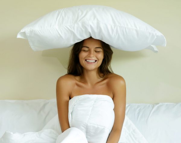 Beautiful happy woman with a pillow on her head in the bedroom